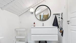 A modern bathroom with a white vanity, a round mirror, a towel rack, and a shower area visible through the glass door. - 3 bedroom stunning home in Ringkøbing (Ringkøbing)