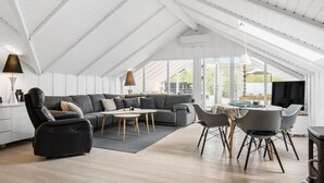 A modern living room with a sectional sofa, a dining table, and chairs. - 3 bedroom stunning home in Ringkøbing (Ringkøbing)