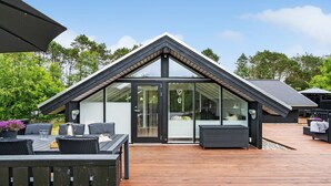 Een modern huis met een schuin dak, grote glasramen en een houten terras.