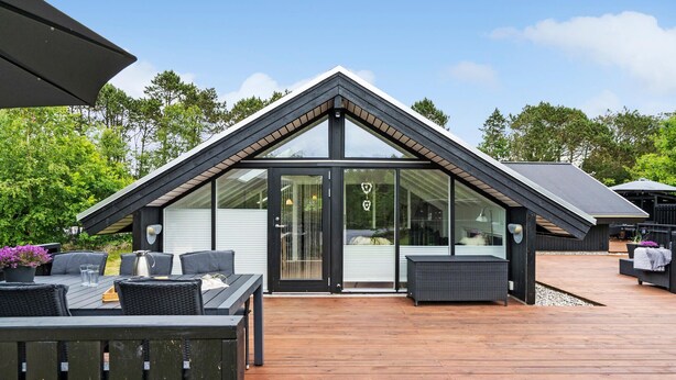 A modern house with a sloped roof, large glass windows, and a wooden deck. - 3 bedroom stunning home in Ringkøbing (Ringkøbing)