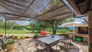Una veranda esterna con tavolo e sedie in pietra, un barbecue e una tenda rossa sullo sfondo.