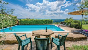 Una piscina con vista sul mare, circondata dal verde e da un patio in pietra con tavolo e sedie.