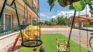 Zona infantil con un trampolín, un conjunto de columpios y una pequeña tienda de campaña.
