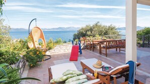 A patio with a view of the sea, a swing, a slide, and outdoor furniture.