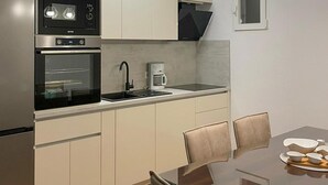 A modern kitchen with a built-in oven, a coffee maker, and a dining area with a glass table and chairs.