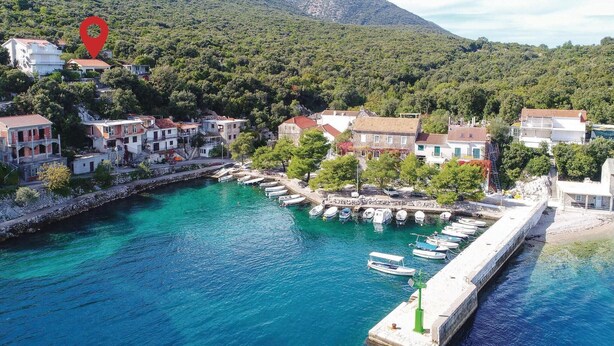 A coastal village with a marina, stone buildings, and a mountainous backdrop.