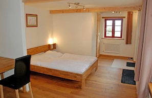 A room with a wooden bed, a desk, a chair, a radiator, and a window with curtains. - 06 Holiday apartment Bauernrose with lake view - Haus am Höft in Gager with lake view (Gager)