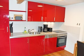 Eine kleine Küche mit roten Schränken, einem Geschirrspüler, einem Backofen, einer Kaffeemaschine und einer Mikrowelle.