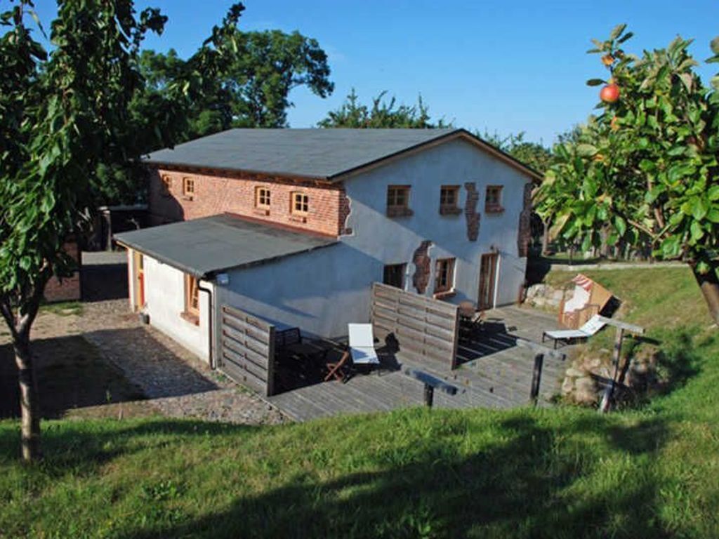 Ein zweistöckiges Haus mit Backsteinfassade und weiß verputzter Vorderseite, einer Holzterrasse und einem kleinen Garten.