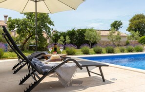 Zona de piscina amb una cadira relaxant, una ombra i una ampolla de vi sobre una taula.