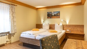 Una habitación con cabecera de madera, cama con sábanas blancas y almohadas amarillas, una mesa de madera y una silla.
