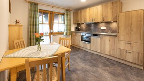 Una cocina con armarios de madera, una mesa de comedor con sillas y una ventana con cortinas.