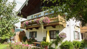 Una cabaña tradicional con un balcón decorado con flores colgantes, una valla de madera y un jardín con diversas plantas y flores.