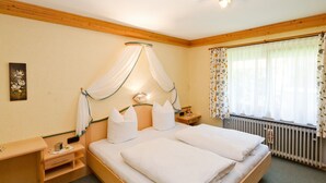 A neatly made double bed with a canopy, a bedside table with a lamp, and a window with floral curtains. - Apartment Rauschberg 67sqm, balcony, kitchenette, 2 bedrooms, 1 living room (Ruhpolding)
