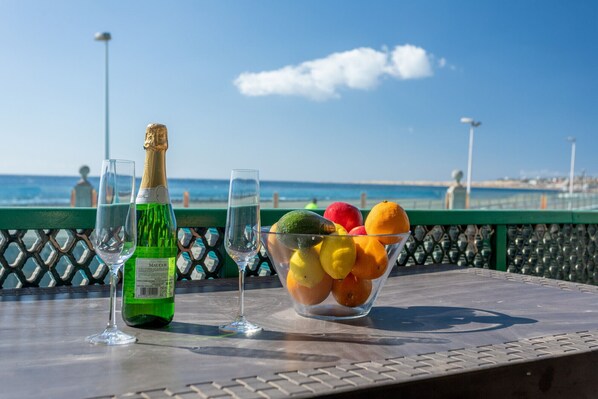 Een tafel met een champagnefles, twee glazen en een schaal fruit met uitzicht op zee.