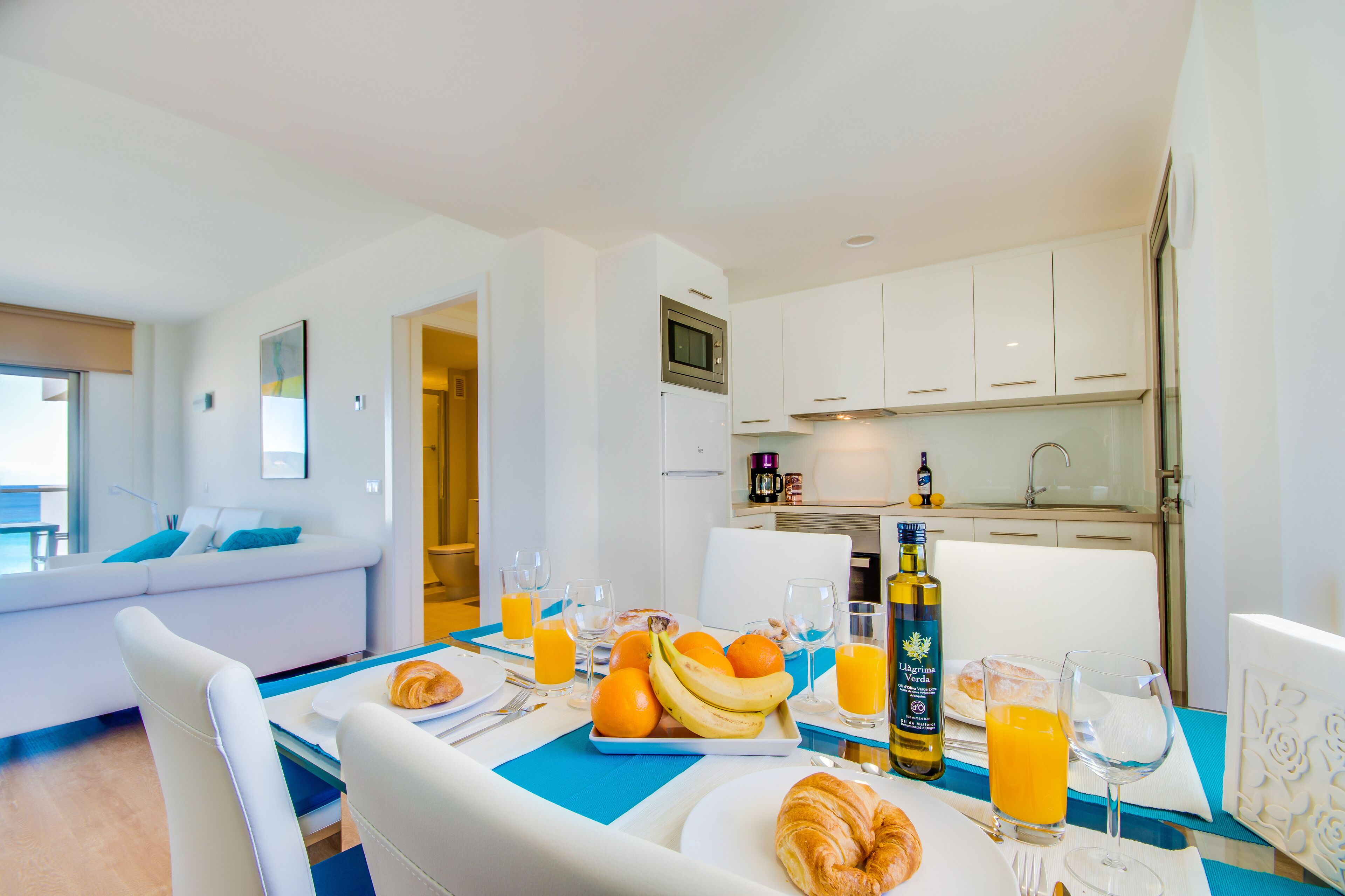 Habitación de hotel moderna con zona de comedor que presenta una mesa dispuesta para el desayuno, con croissants, fruta y jugo de naranja.