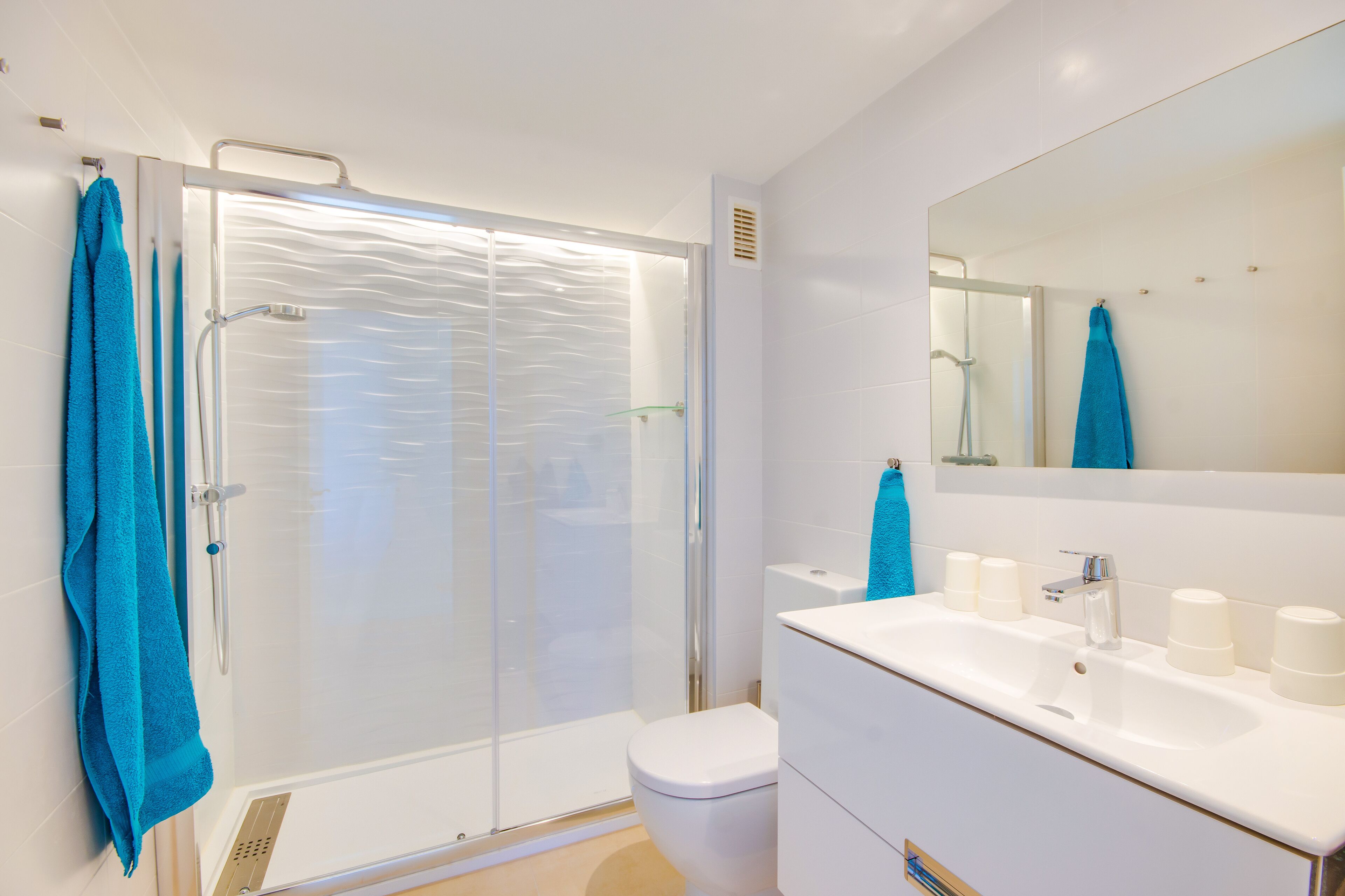 A modern bathroom with a glass-enclosed shower, a white sink with multiple soap dispensers, and a large mirror above the sink.