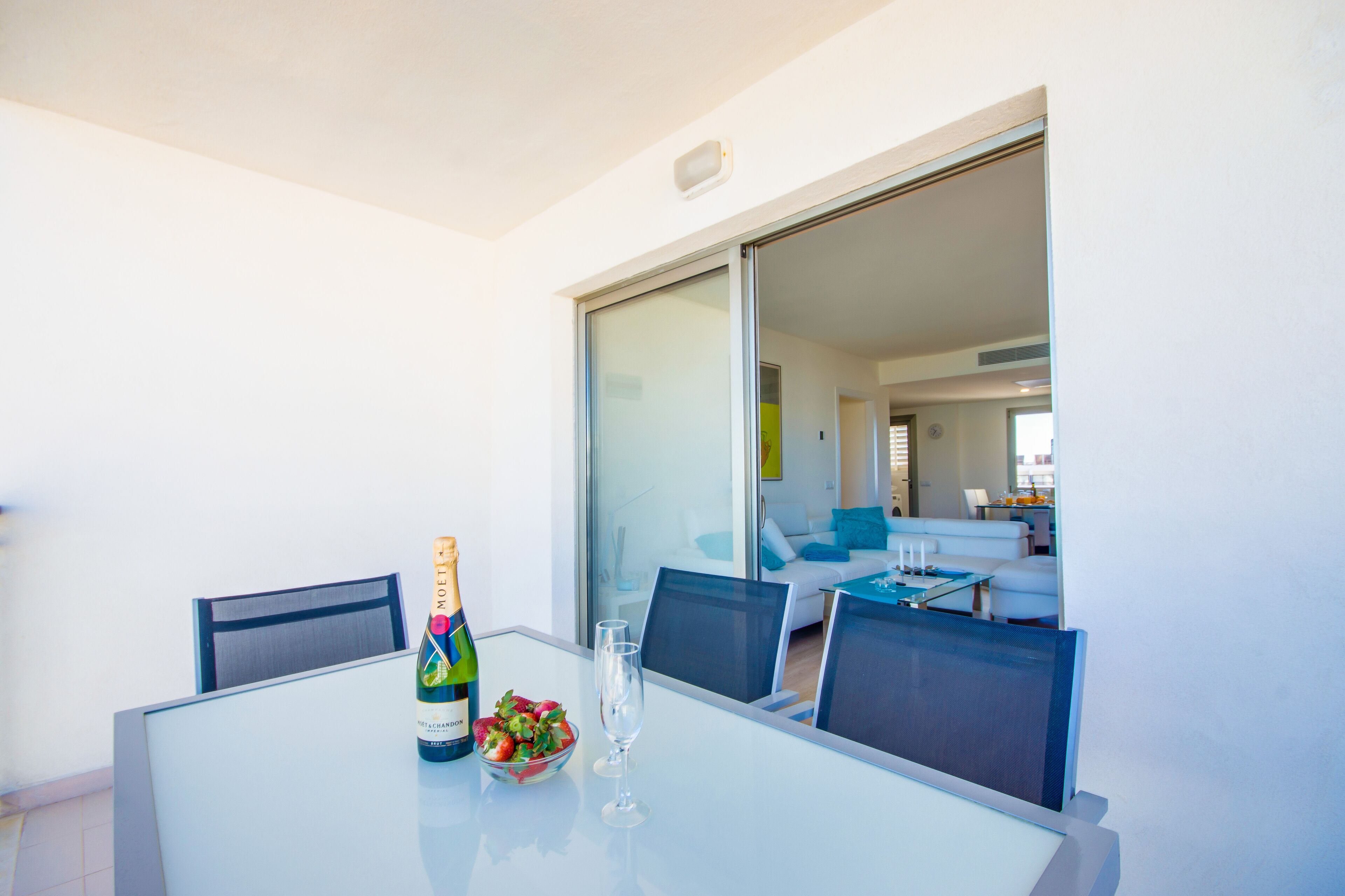 A dining area with a table, chairs, a bottle of champagne, and a bowl of fruit.