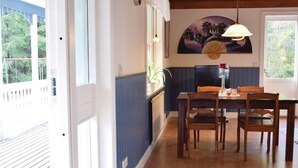 A dining area with a wooden table and chairs, a painting on the wall, and a window with a view of trees. - 3 bedroom stunning home in Slite (Slite)