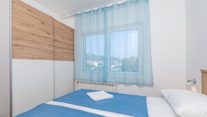 A bedroom with two beds, a window with a sheer curtain, a radiator, and a view of buildings outside. - 1 bedroom amazing apartment in Rab (Rab)