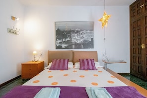 A bedroom with a bed, a nightstand, a star-shaped hanging light, a wall-mounted picture, and a wooden door.