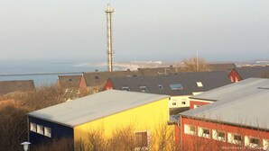 Een kustplaats met industriële gebouwen, een hoge zendmast en uitzicht op zee.