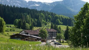 A mountain village with traditional wooden houses, a central building with a sloped roof, and a backdrop of snow-capped peaks.
