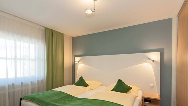 A neatly arranged hotel room with a large bed, two bedside tables, and a headboard with integrated lighting.