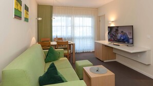 A modern living room with a green sofa, a dining table, and a TV mounted on the wall.