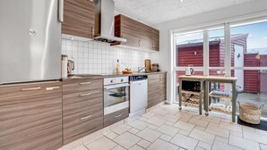 A modern kitchen with a large island, stainless steel appliances, and a view of a red building through the windows.