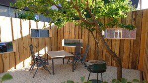 A wooden deck with a table and chairs, a barbecue grill, and a tree providing shade. - Apartment on the market square (Biesenthal)