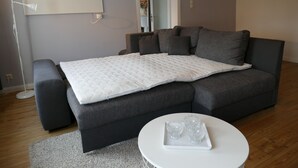 A modern bedroom with a grey sofa bed, a white bedside table with glasses, and a mirror above the bed. - Apartment on the market square (Biesenthal)