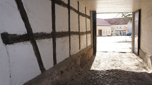 A narrow cobblestone alleyway with a white wall featuring dark timber framing. - Apartment on the market square (Biesenthal)