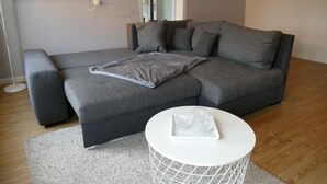 A modern living room with a grey sectional sofa, a white round coffee table, and a grey throw blanket. - Apartment on the market square (Biesenthal)