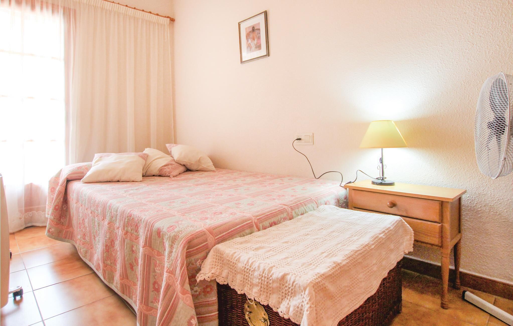 Ein Schlafzimmer mit einem Bett, einem Nachttisch, einer Lampe und einem Wandventilator.