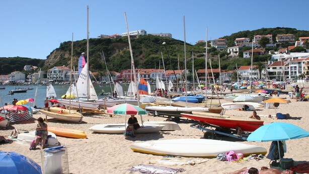 Ein Strand mit vielen Booten, Sonnenschirmen und Menschen.