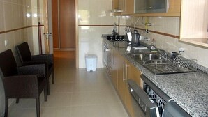 Eine moderne Küche mit einer Granitabdeckung, Edelstahlgeräten und einem eingebauten Backofen. Ein Essbereich mit Korbstühlen und einem kleinen weißen Mülleimer.