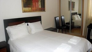 Ein Hotelzimmer mit einem großen Bett, einem Nachttisch, einem Sessel, einem Schreibtisch und einem Spiegel.