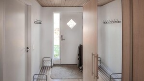 Un couloir étroit avec une porte donnant sur une pièce, une petite fenêtre et des étagères métalliques fixées aux murs.