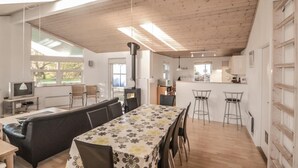 Une cuisine moderne avec un îlot central, un coin repas agrémenté d’une nappe à motifs floraux et un espace salon confortable avec un canapé et des fauteuils.