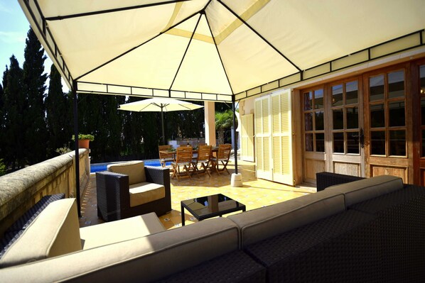 An outdoor patio with a covered seating area, a pool, and a dining set.
