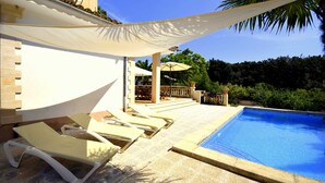 Un espace aménagé au bord de la piscine, avec des chaises longues, un coin salon abrité et une vue sur la végétation environnante.
