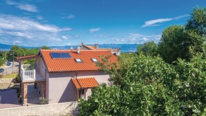 Une maison avec un toit recouvert de tuiles rouges, un balcon et une vue sur les montagnes et la verdure.