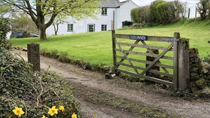 A rural property with a white house, a wooden gate labeled "LLYS ONNEN," and a path leading to the house.