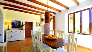 A dining area with a wooden table, white chairs, a basket of oranges, and a wooden ceiling with exposed beams. - 763424 Finca Conies - 763424 Ses Conies (Manacor)