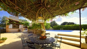 An outdoor patio with a round table and chairs, a hanging light fixture, and a view of a swimming pool. - 763424 Finca Conies - 763424 Ses Conies (Manacor)