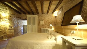 A bedroom with a large bed, a nightstand, a lamp, a radiator, and stone walls. - 763424 Finca Conies - 763424 Ses Conies (Manacor)