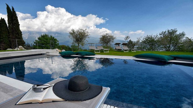 Piscina cristallina blu con sedie a sdraio e un libro, che riflette il cielo e le nuvole.