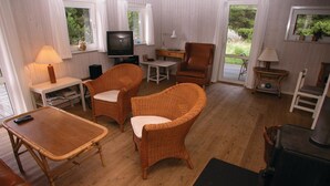 Uma sala de estar aconchegante com móveis de vime, uma televisão, lareira e vista para o exterior.