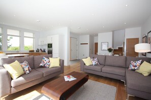 A modern living room with two sofas, a coffee table, and a kitchen in the background. - Beautiful holiday home with hot tub, just a walk away from Talland beach... (Looe)